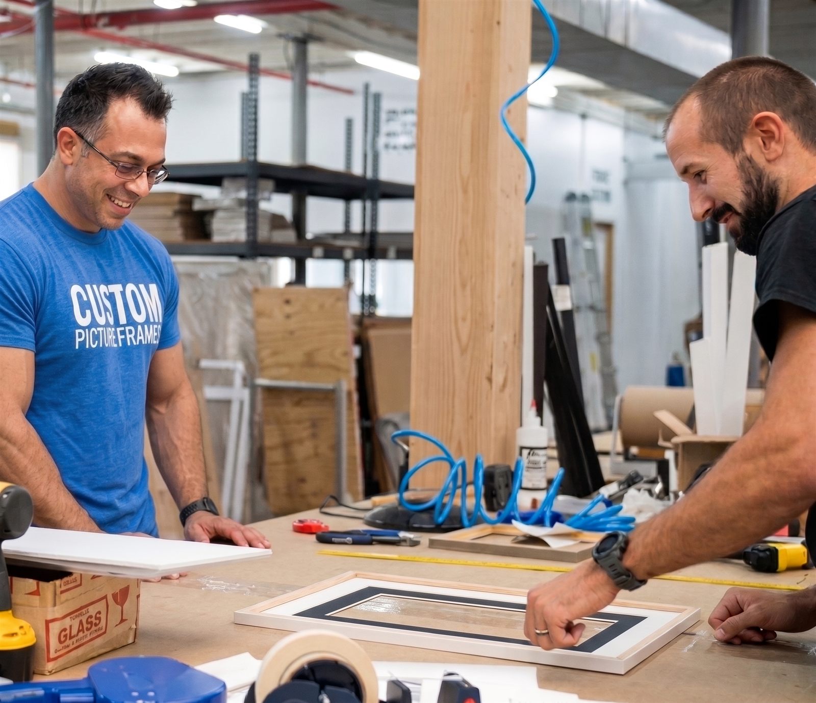 Two smiling framers fitting a mat into a frame at the workbench in the Somerset shop